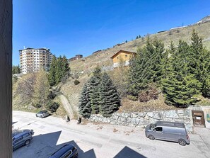 A residential area with a road, parked cars, and a hillside with trees and buildings. - Economical studio for 2 in Reberty 1850, near slopes (Les Menuires)