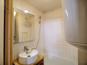 Bathroom features a large mirror, vanity with sink, and a shower area with tub.