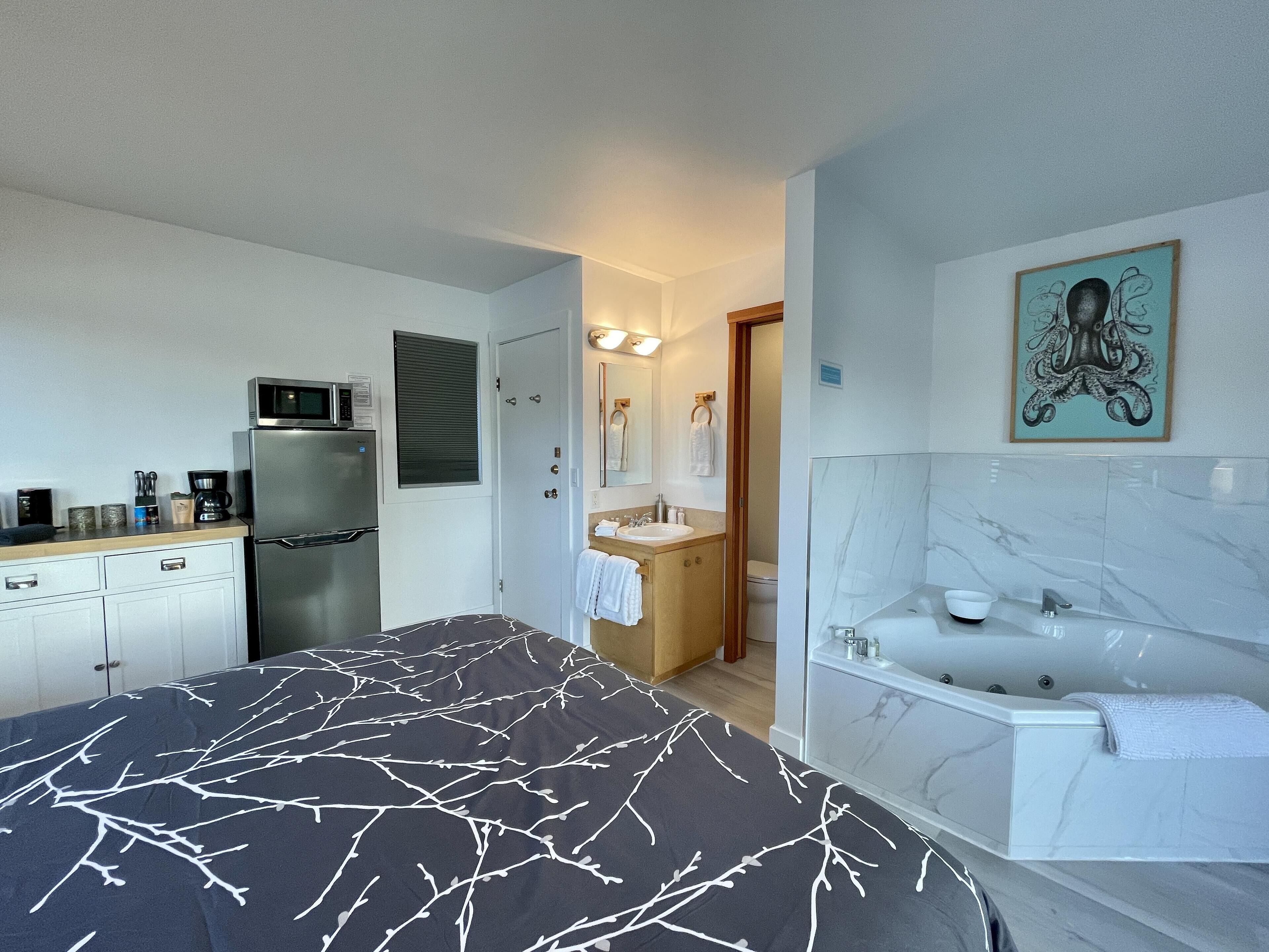 Una habitación de hotel compacta con cama, kitchenette, baño y un cuadro en la pared.