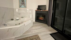 A modern bathroom with a marble sink, a large bathtub, a fireplace, and a television on a shelf.