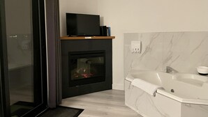 A modern bathroom with a fireplace, a bathtub, and a television on a shelf. - Sea Esta (Ucluelet)