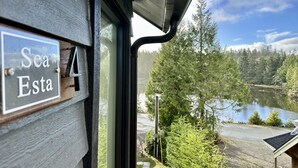 A view from a window with a sign reading "Sea Esta" and a lake with trees and a building in the background. - Sea Esta (Ucluelet)