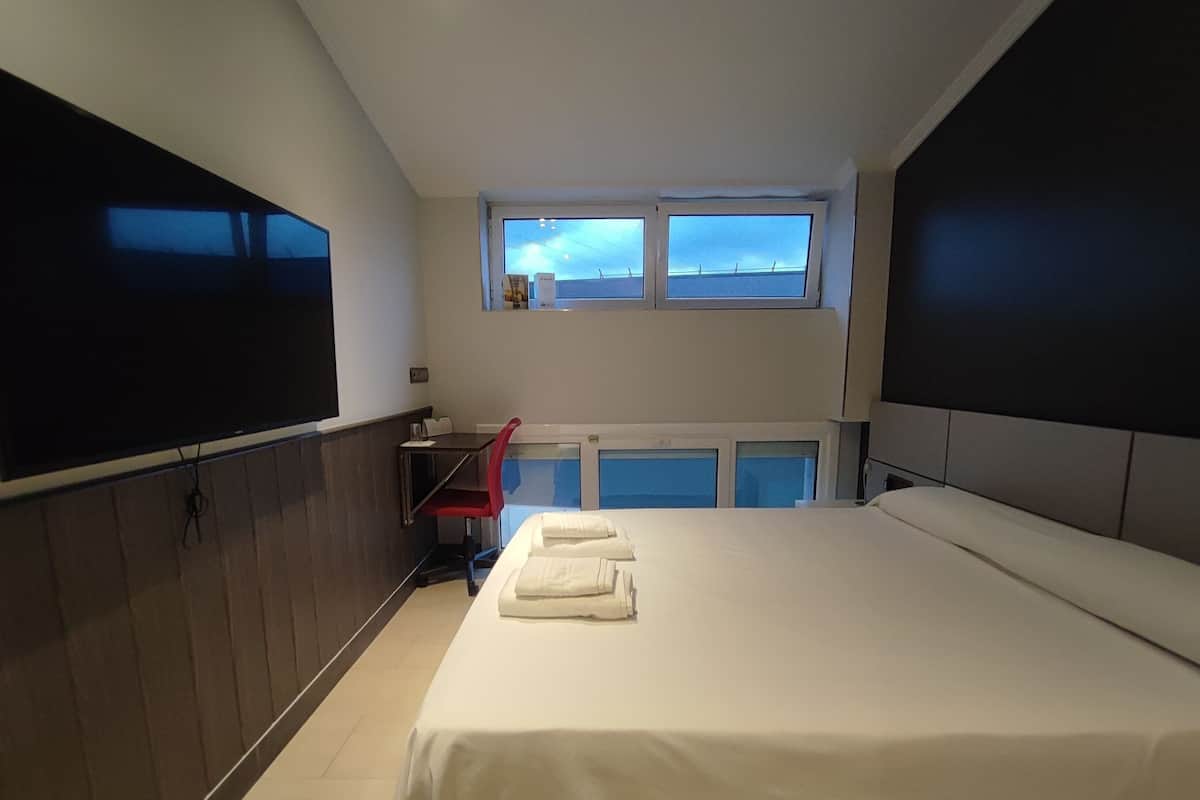 A hotel room with a bed, a desk, a chair, and a TV.