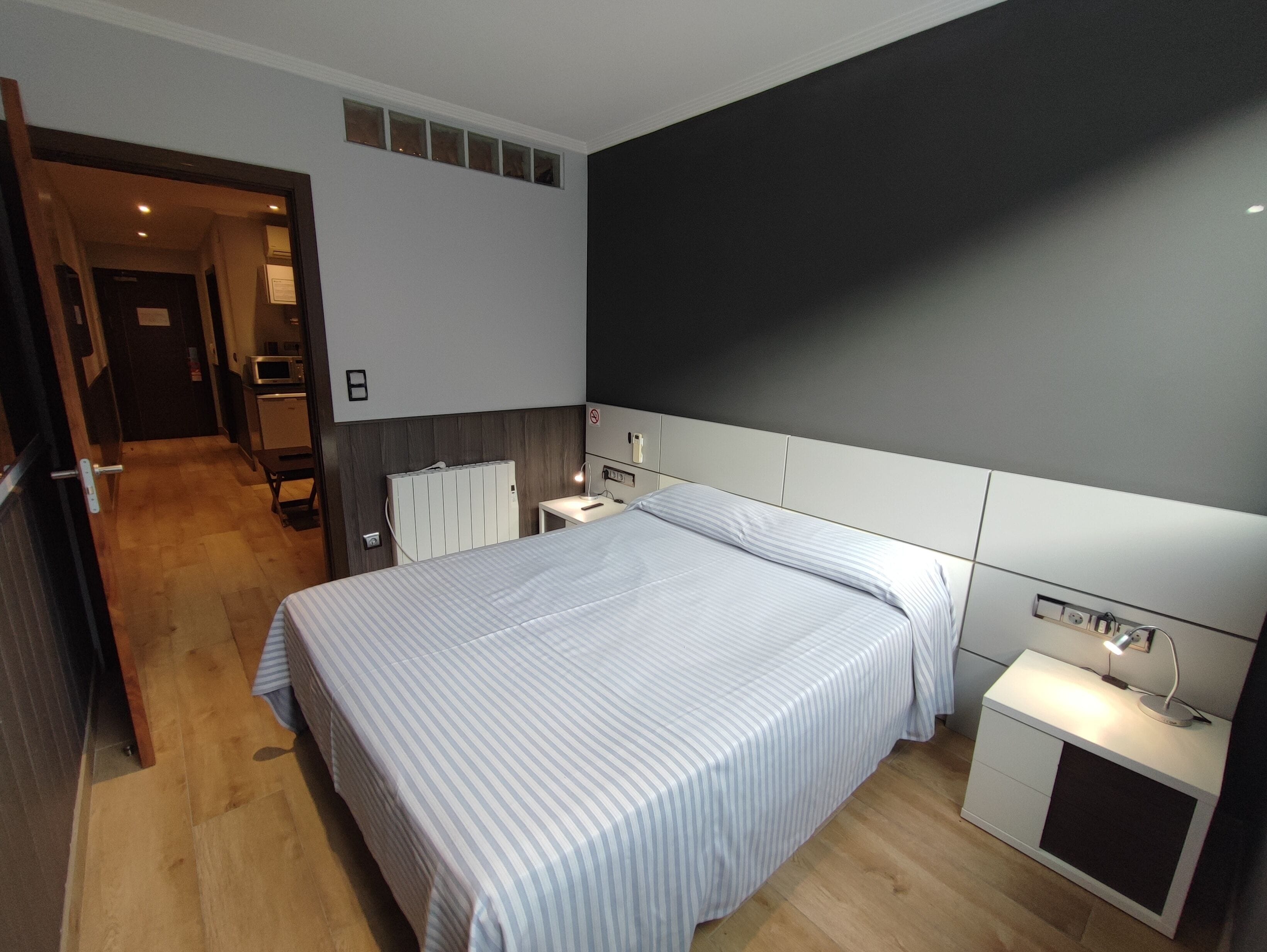 A modern hotel room with a large bed, bedside tables, a desk, and a wardrobe.