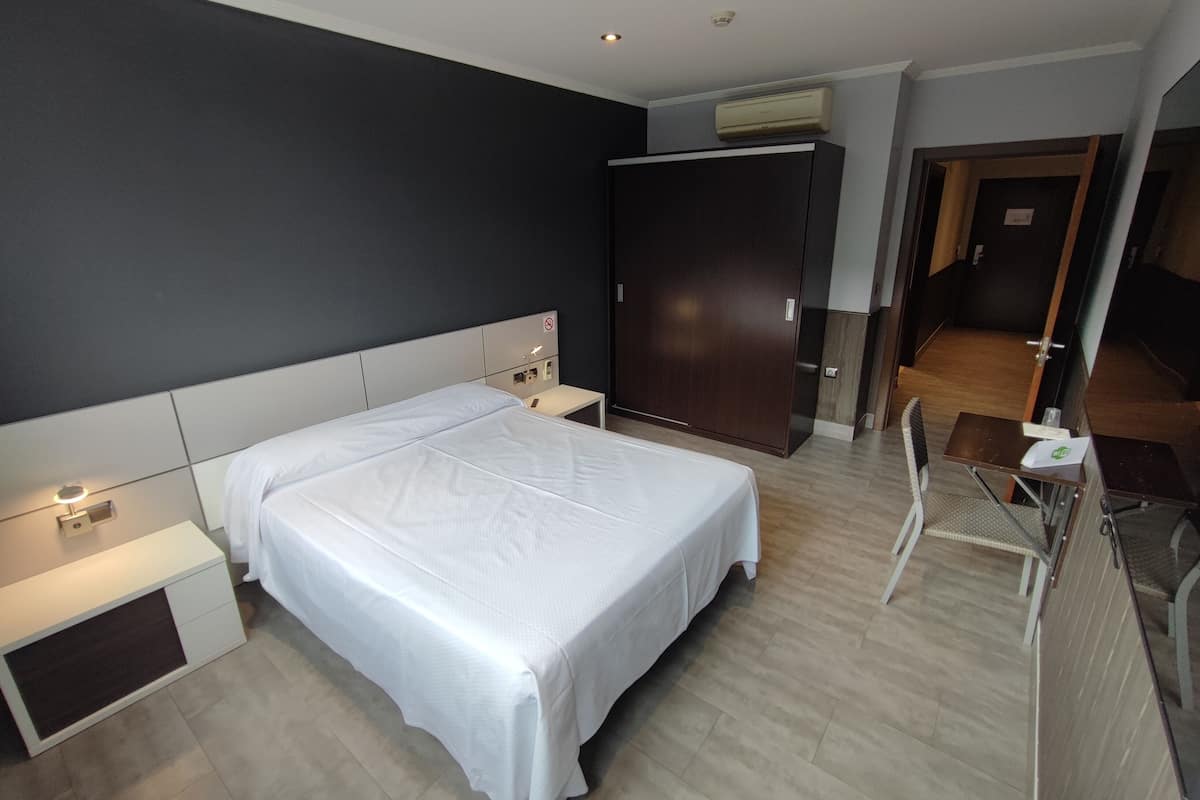 A hotel room with a bed, bedside tables, a wardrobe, and a desk with a chair.