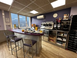 Una barra de desayuno con asientos, una máquina de café y un reloj en la pared.