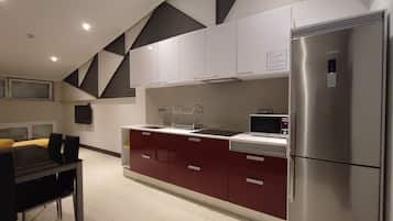 Una cocina moderna con electrodomésticos de acero inoxidable, armarios blancos y burdeos, y un comedor con mesa y sillas.