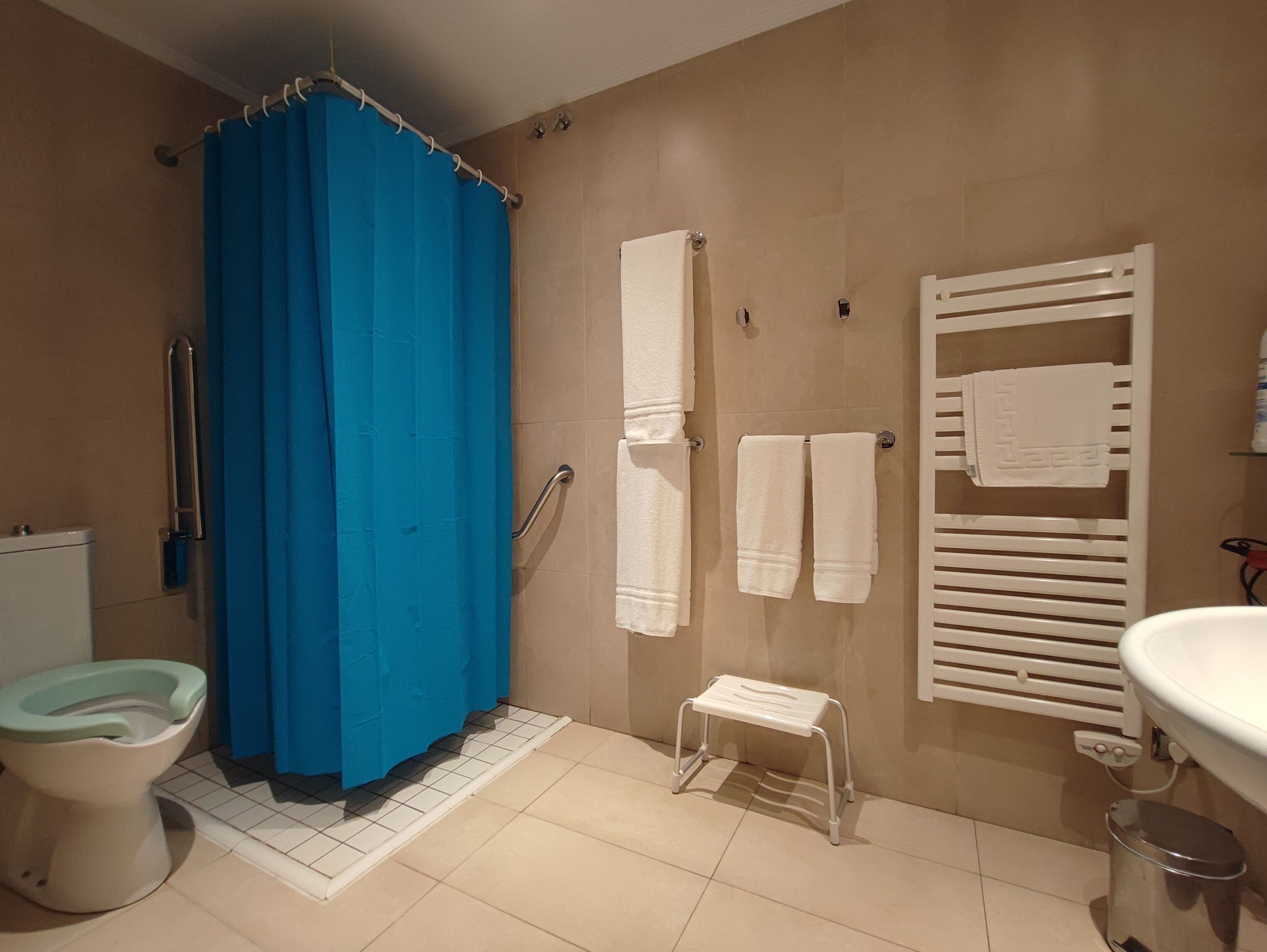 Ein Badezimmer mit Toilette, einer Dusche mit blauer Duschvorhang, einer kleinen weißen Stehgehocker und einem Handtuchhalter mit Handtüchern.