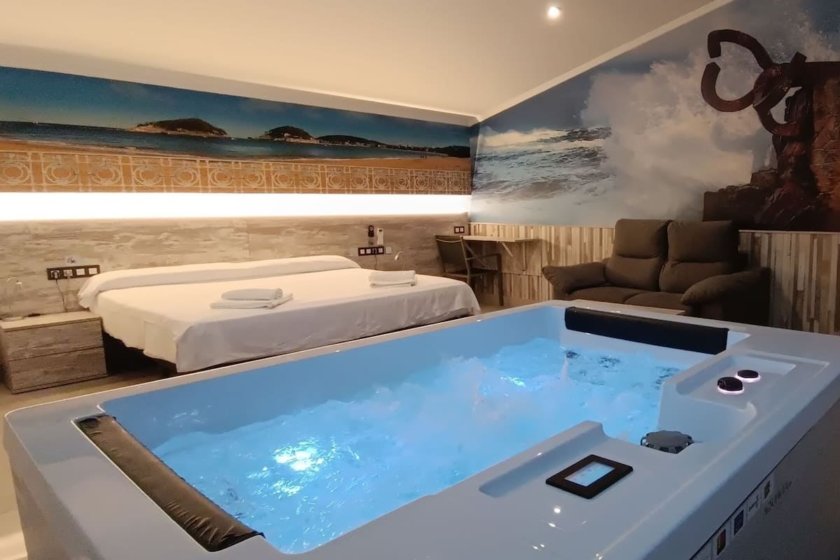 A room with a large bathtub, a bed, a massage table, and a chair.