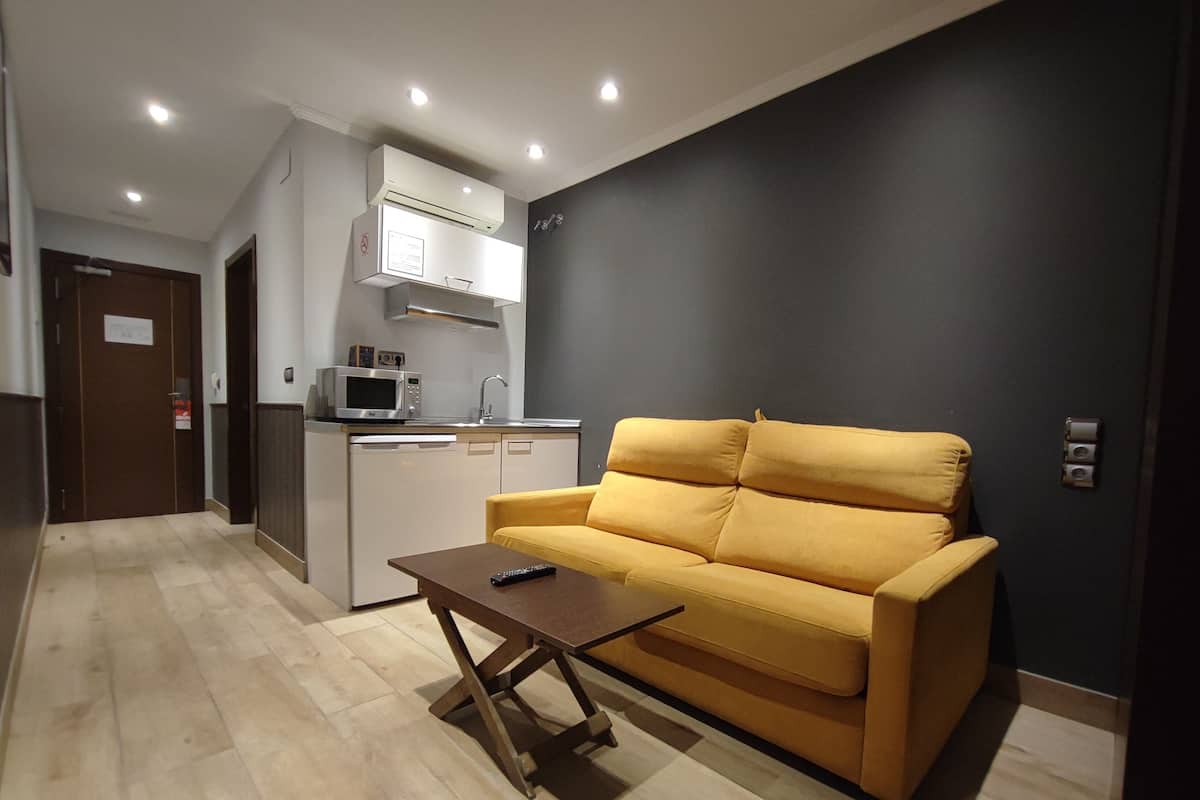 A compact living space with a kitchenette, a yellow sofa, a coffee table, and a dark-colored wall.
