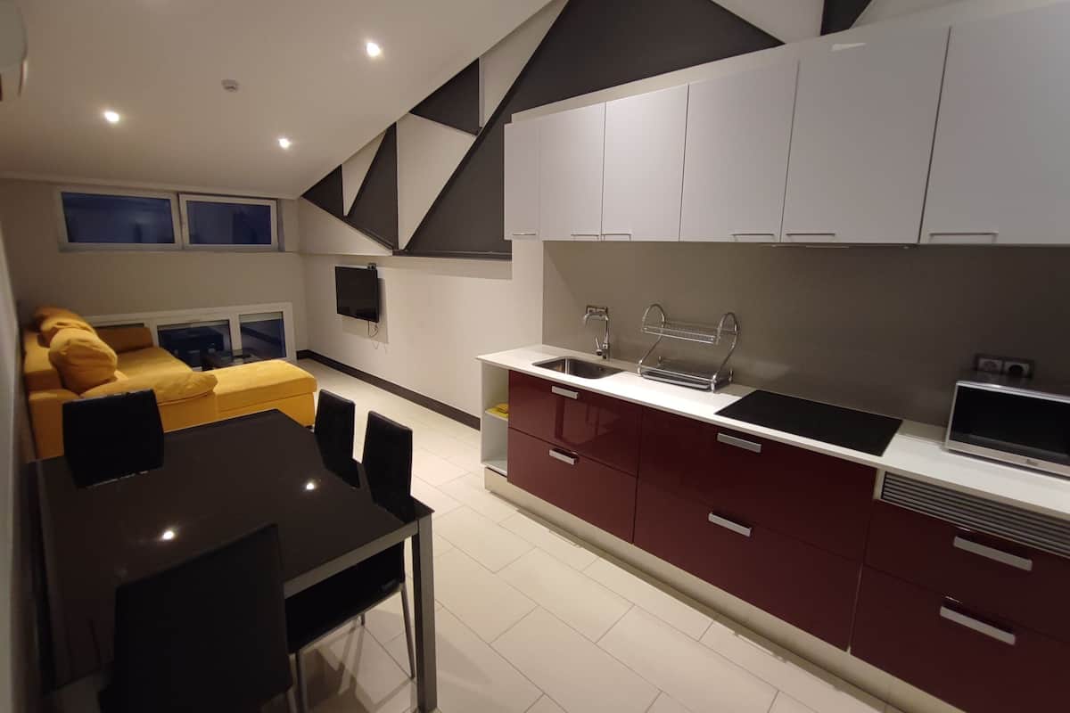 A modern kitchen with white and red cabinets, a black dining table, and a yellow sofa in the living area.