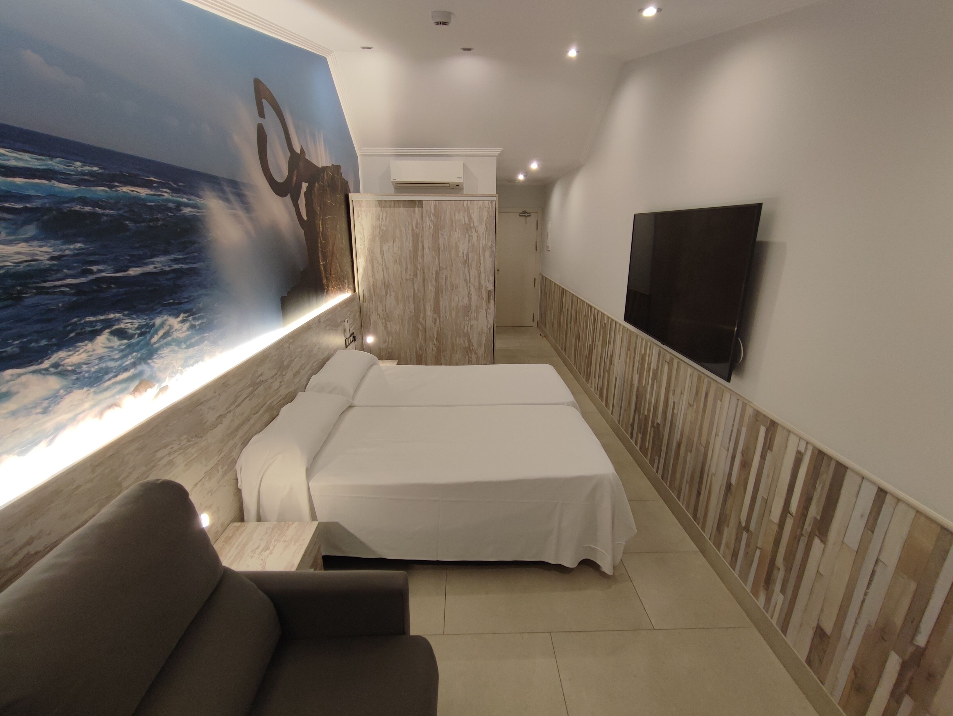 A hotel room with a large ocean mural, two beds, a flat-screen TV, and a seating area.