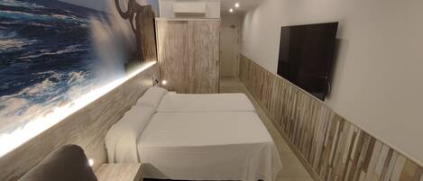A hotel room with a large ocean mural, two beds, a flat-screen TV, and a seating area.