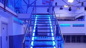 Una escalera con iluminación azul, barandillas de metal y suelo de baldosas.