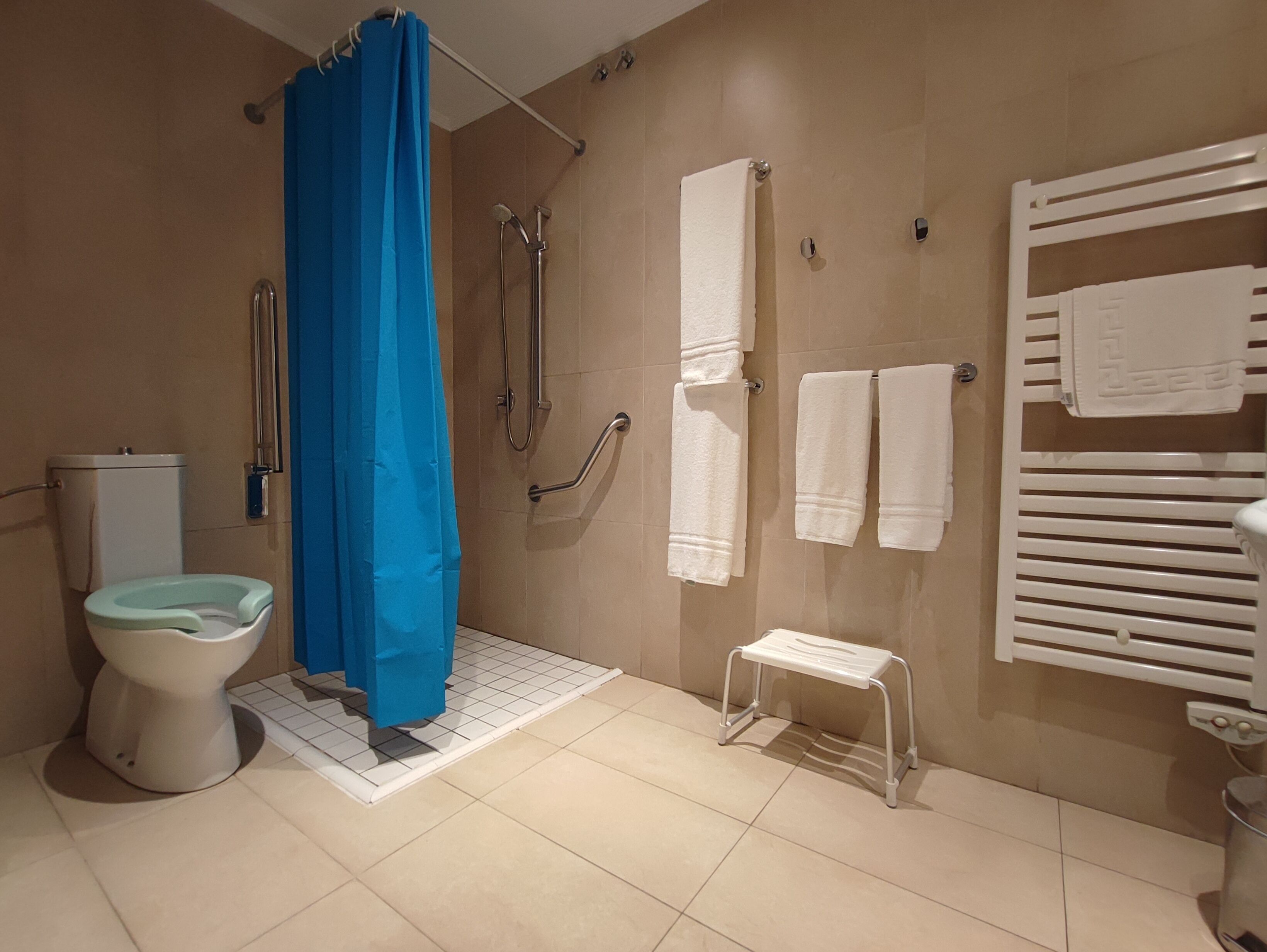 Un baño con ducha, inodoro y un pequeño taburete blanco.