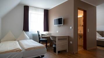 A hotel room with two beds, a desk, a TV, and a bathroom visible through an open door.