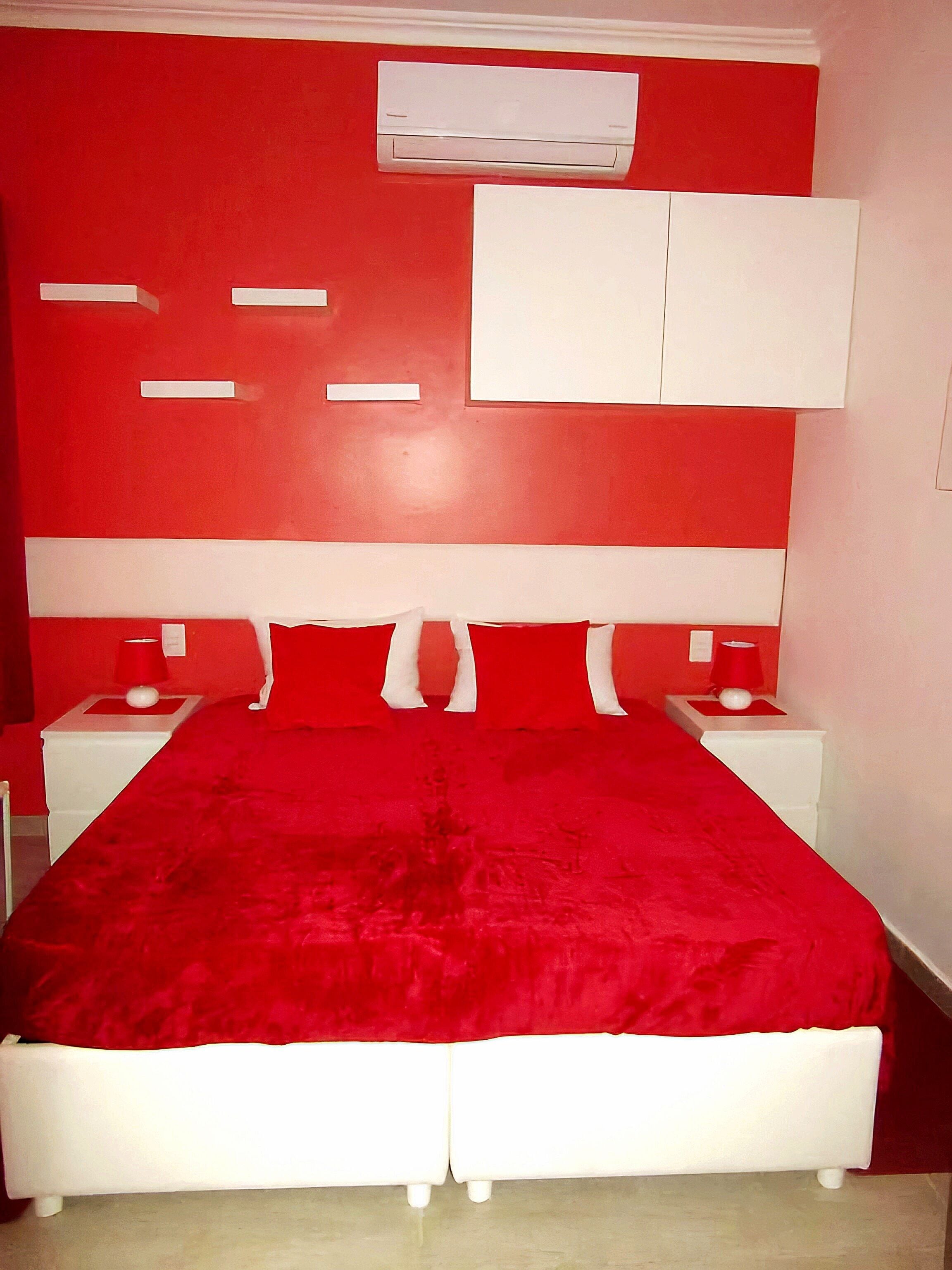 Una stanza con arredamento nei toni del rosso e del bianco, con un letto con copripiumino rosso, testiera bianca e comodini con lampade rosse.