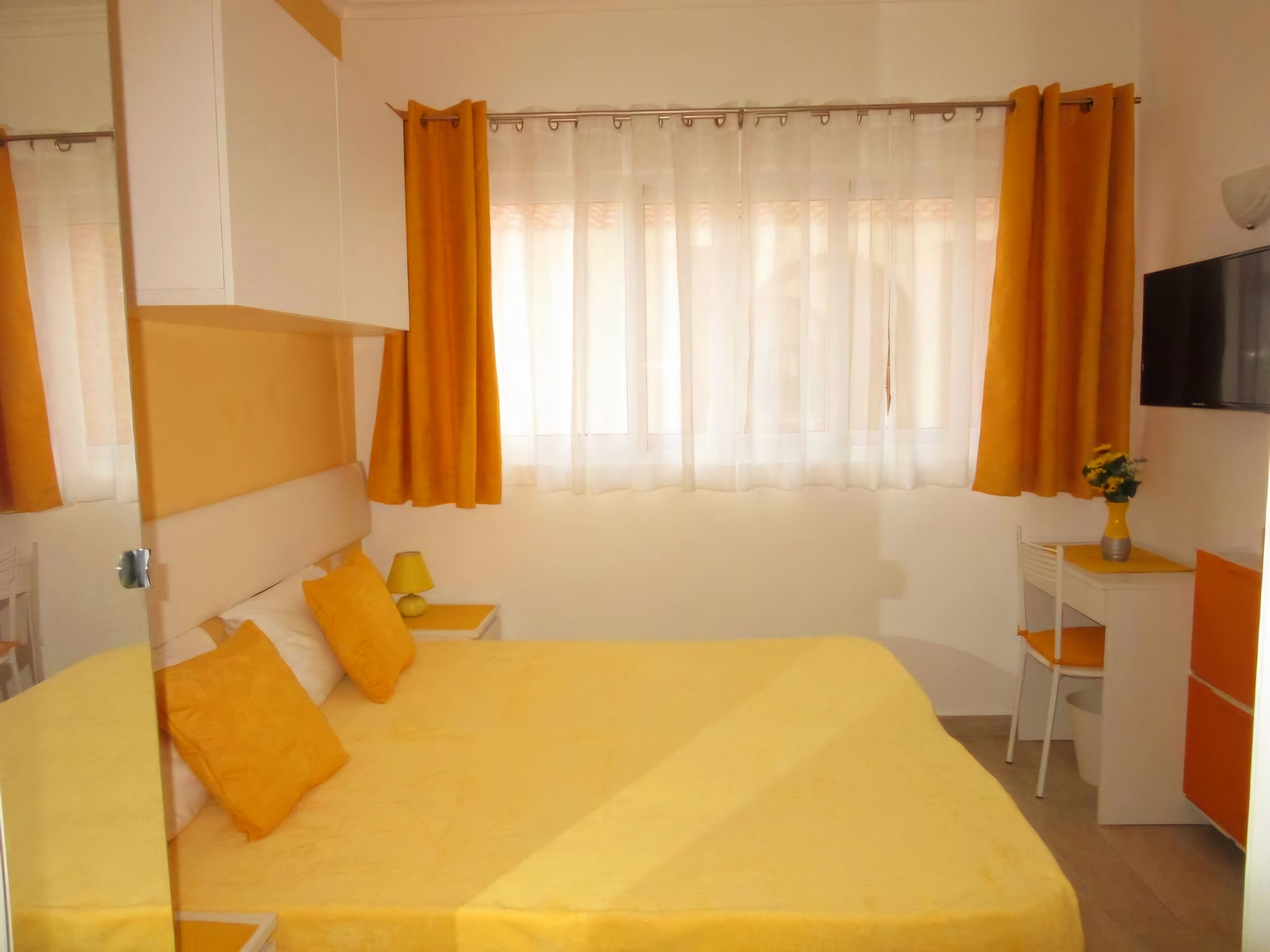 A room with a bed, a desk, a chair, a TV, and a window with curtains.
