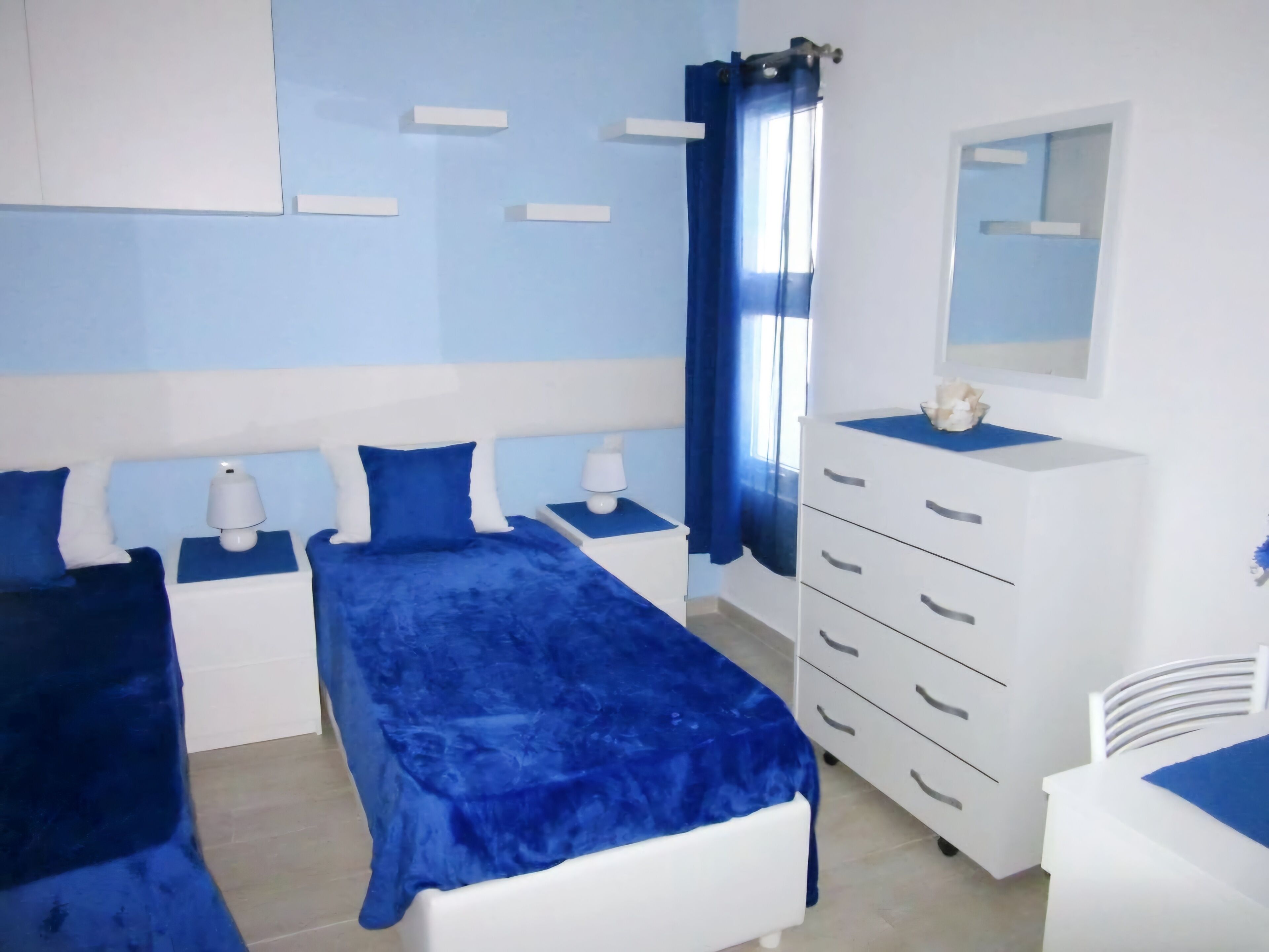 Un dormitorio con dos camas, un aparador, un espejo y una ventana con cortinas azules.