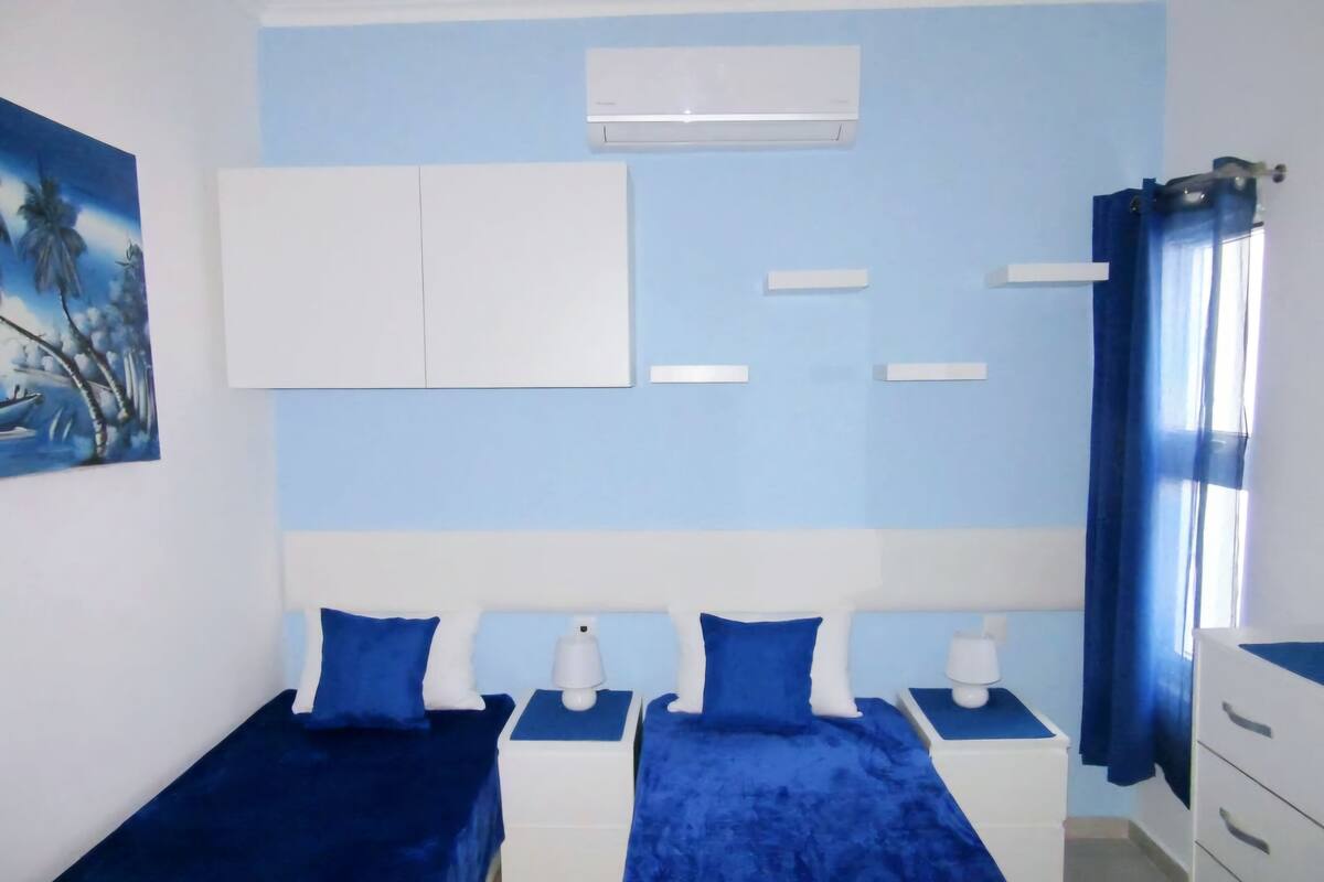 Een slaapkamer met twee bedden, een witte garderobe, een plafondventilator en een schilderij van palmbomen.