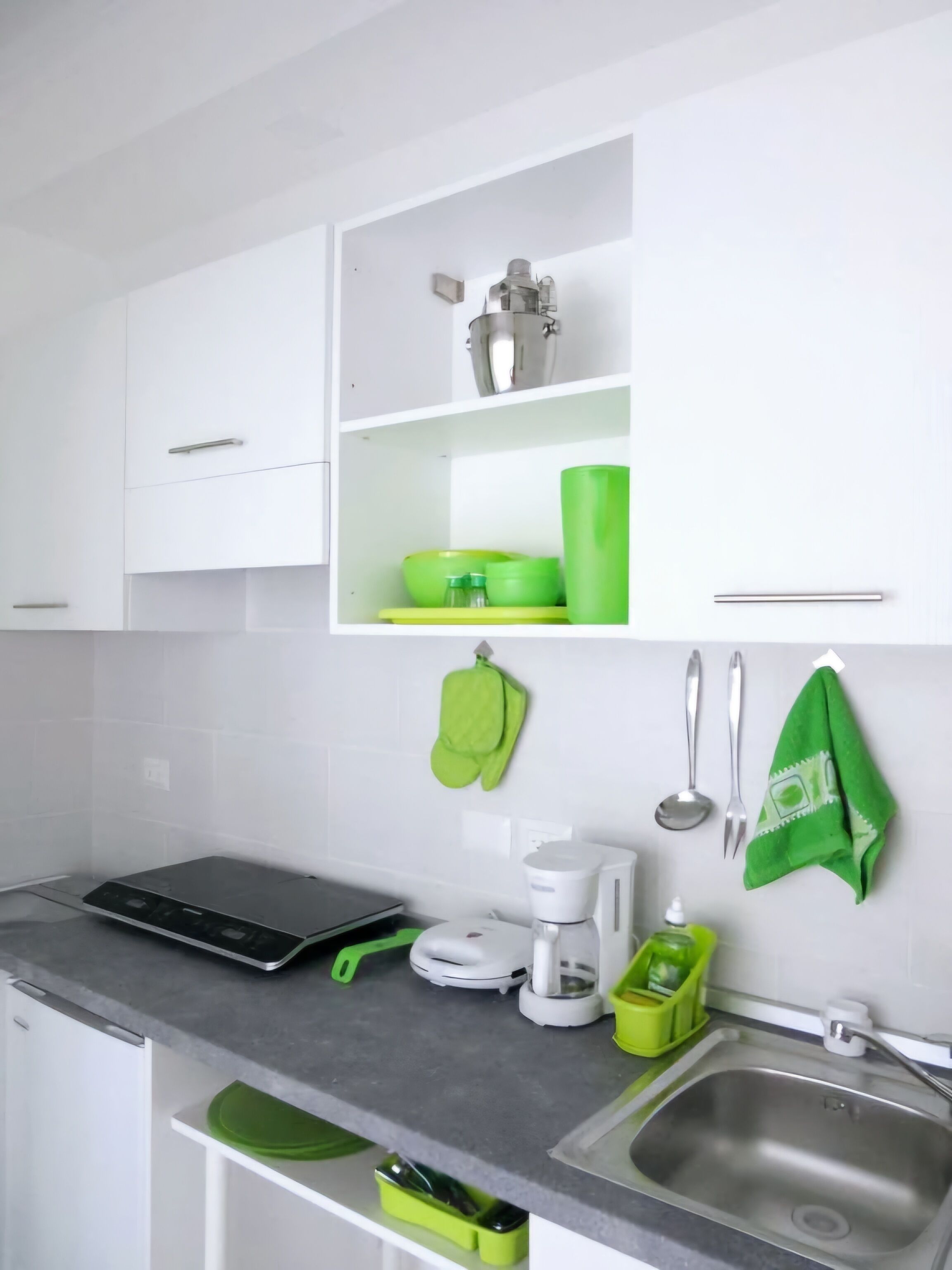 A modern kitchen with white cabinets, a black induction cooktop, a coffee maker, and green kitchen accessories.