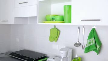 A modern kitchen with white cabinets, a black induction cooktop, a coffee maker, and green kitchen accessories.