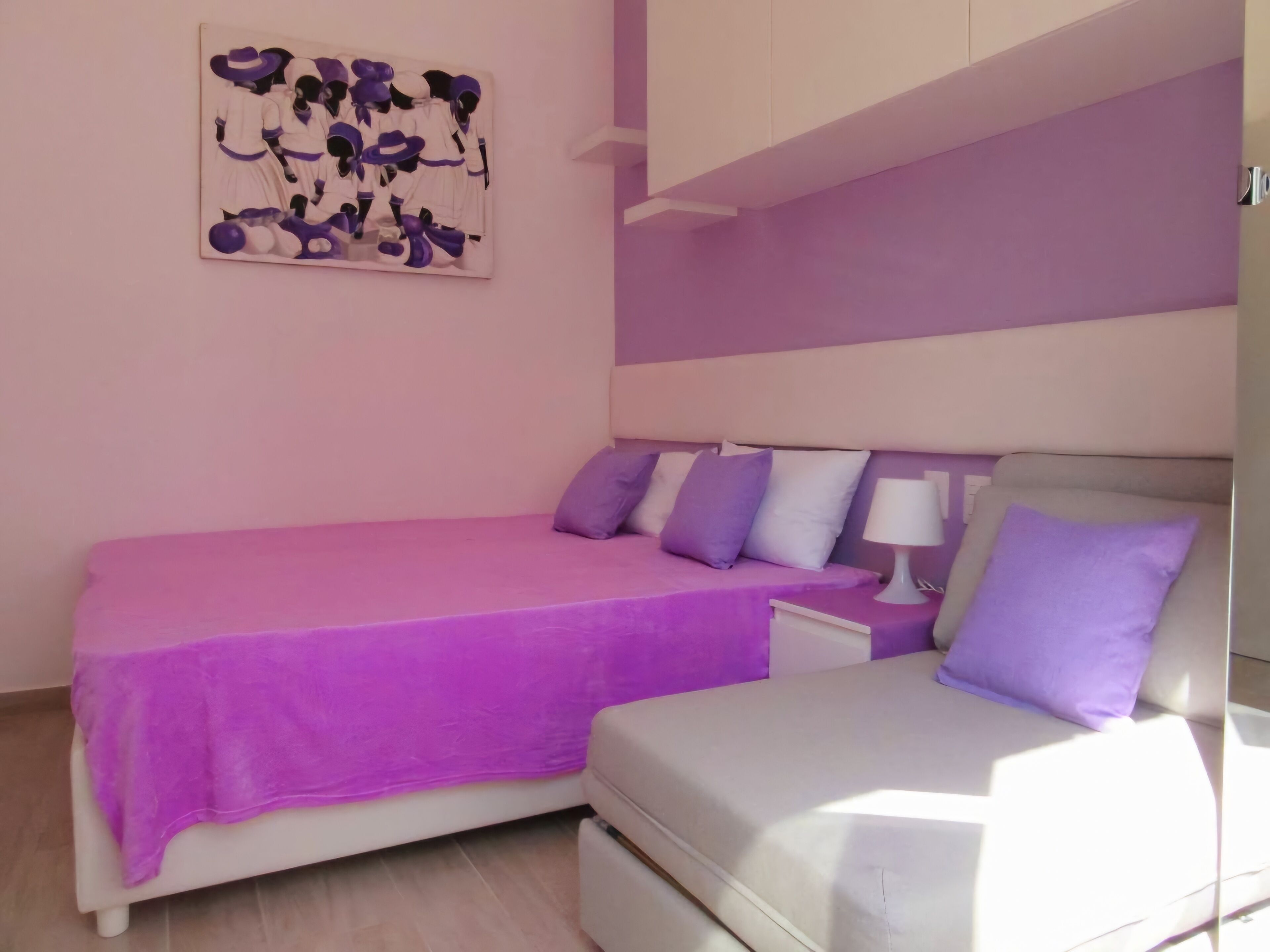 Quarto com cama, mesa de cabeceira, abajur e uma obra de arte na parede.