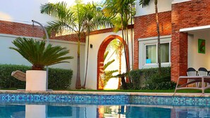 A modern pool area with a clear pool, a brick building, and palm trees.