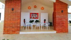 A covered outdoor dining area with a brick wall, white furniture, and hanging lights.