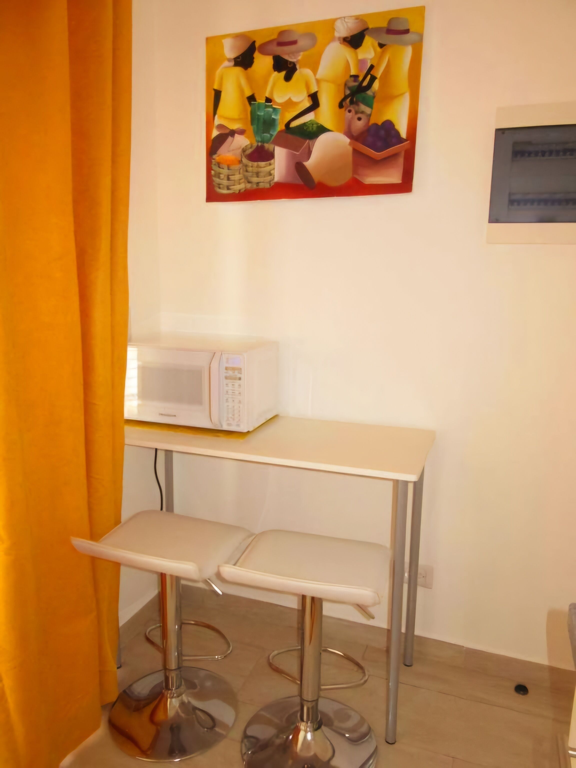 A small kitchenette with a microwave, a white table, and two bar stools.