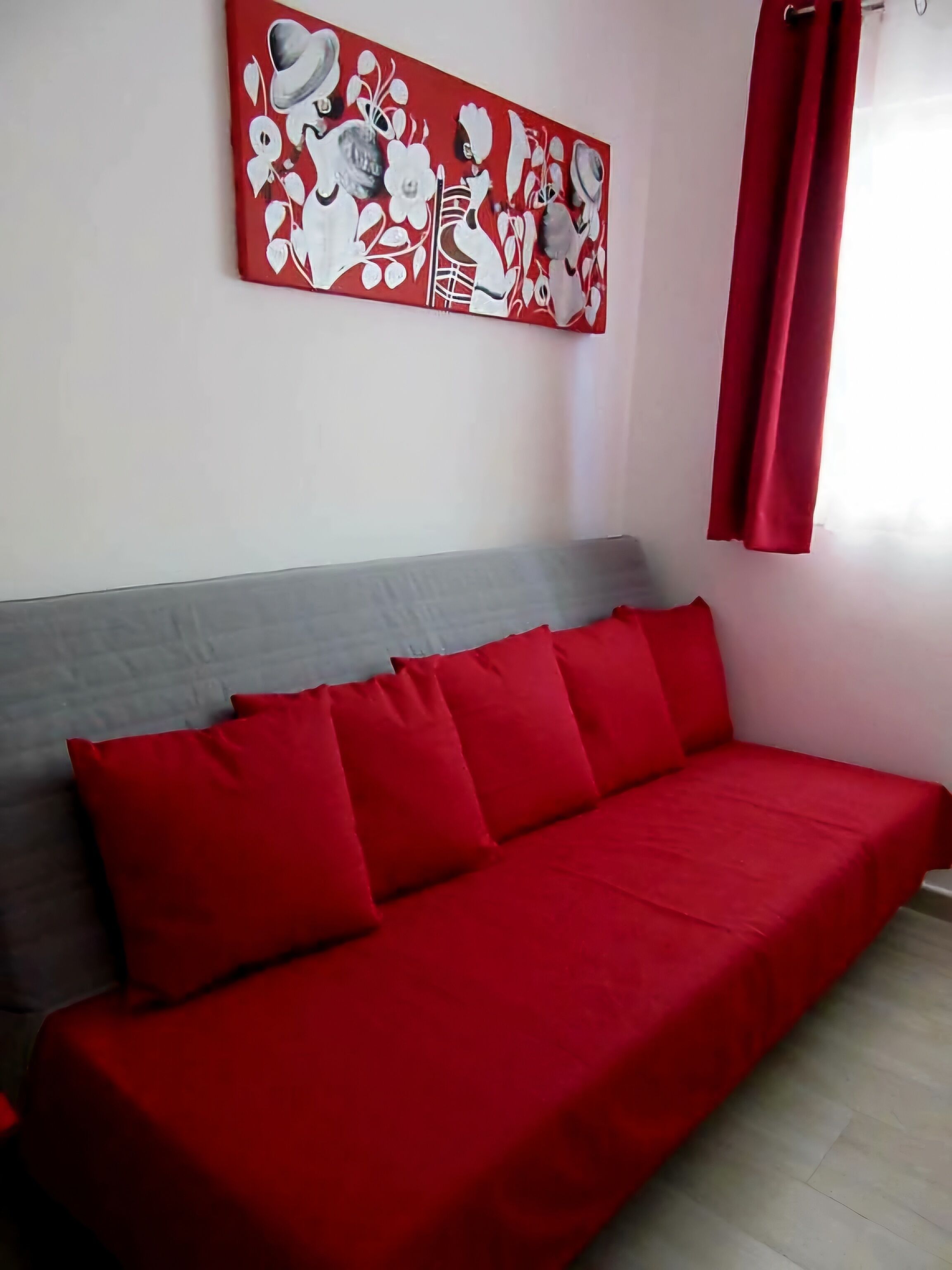 Quarto com sofá vermelho, cabeceira cinza e cortina vermelha.