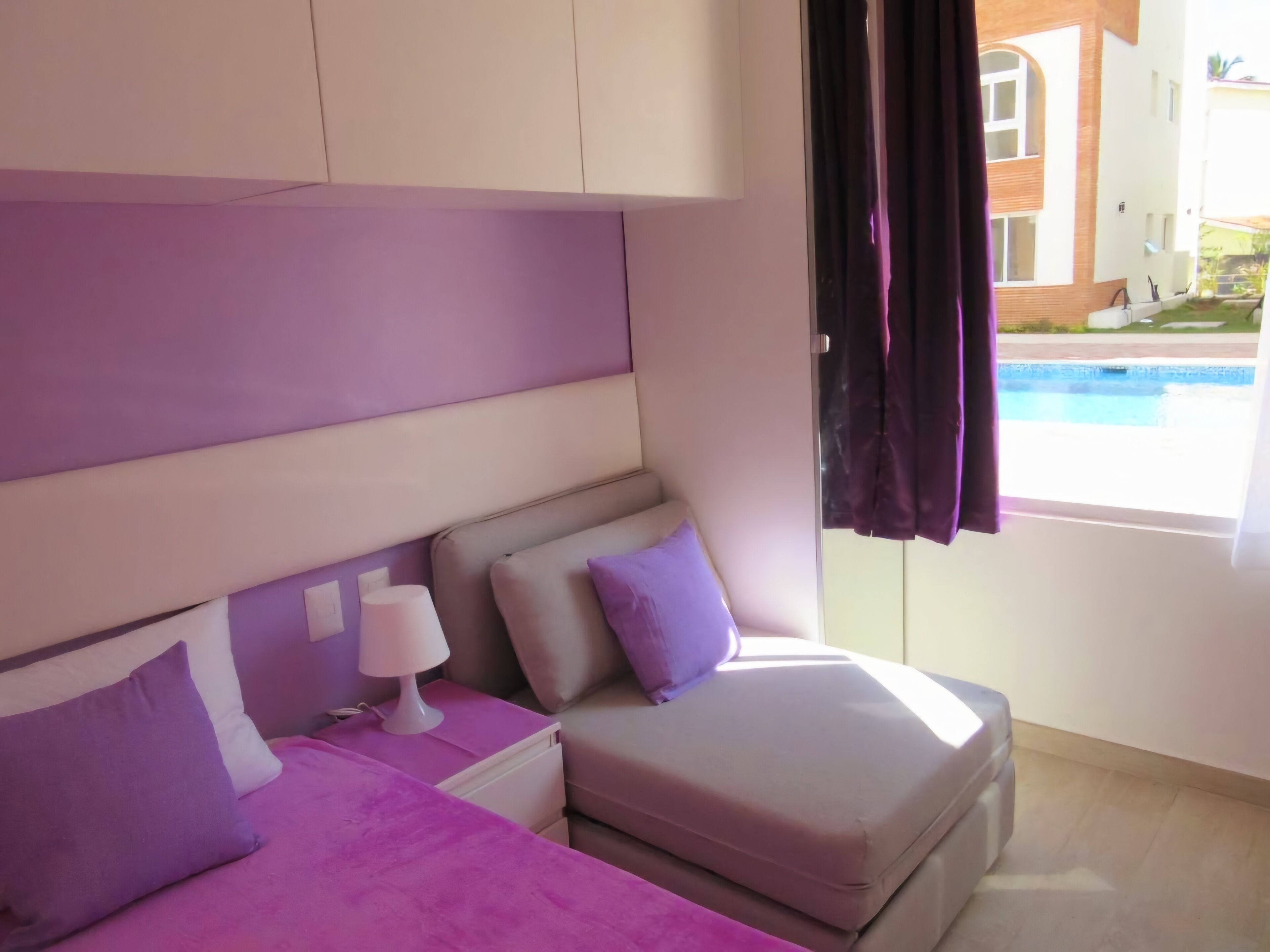 Un dormitorio con dos camas, una mesita de noche y ventana con vista a una piscina.