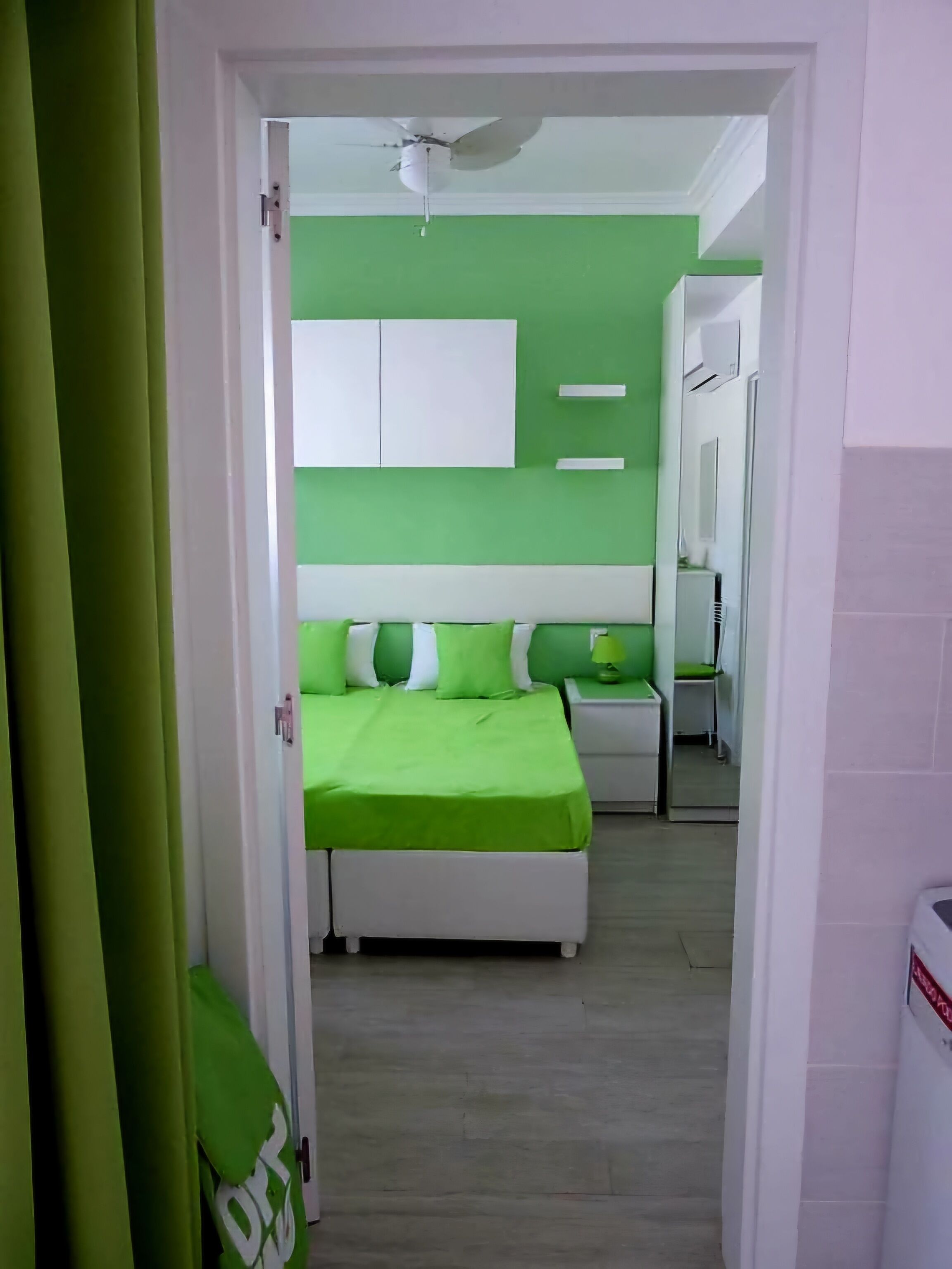 A bedroom with a green bedspread, white headboard, and a ceiling fan.