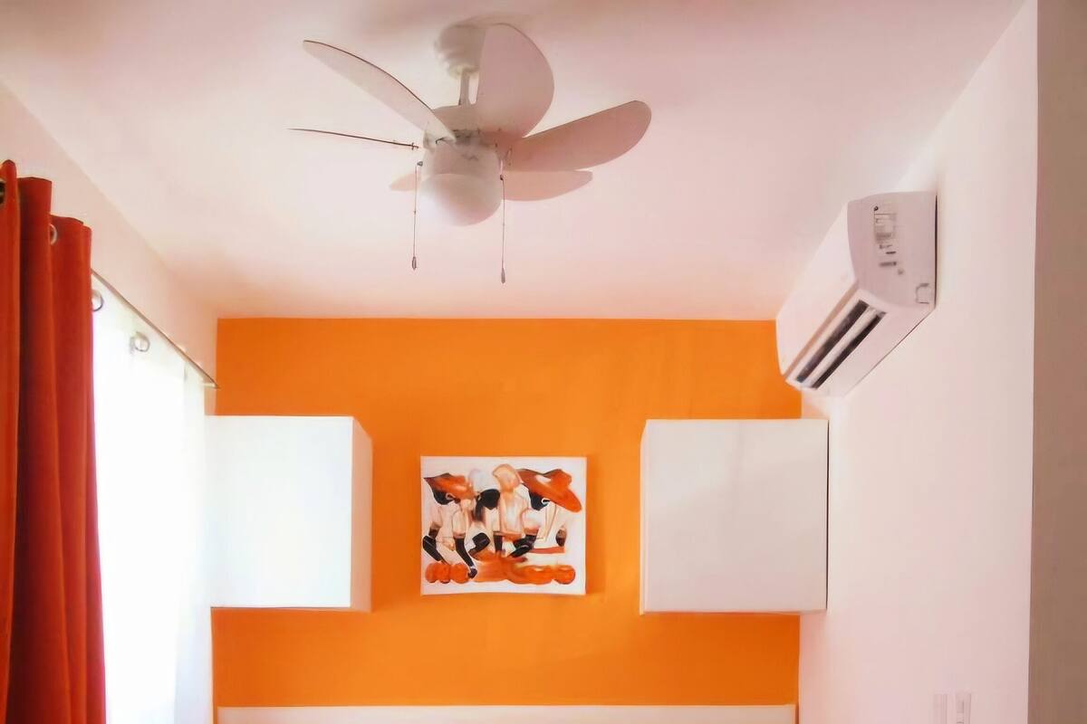 Een hotelkamer met een bed, een plafondventilator, een airconditioner en een schilderij aan de muur.