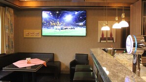 A hotel lobby with a large TV screen displaying a sports event, a bar area with a beer tap, and seating arrangements. - Hotel Restaurant Haus Schieferstein (Dahlem)