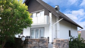 A two-story house with a balcony, stone foundation, and a clear sky. - Hotel Restaurant Haus Schieferstein (Dahlem)
