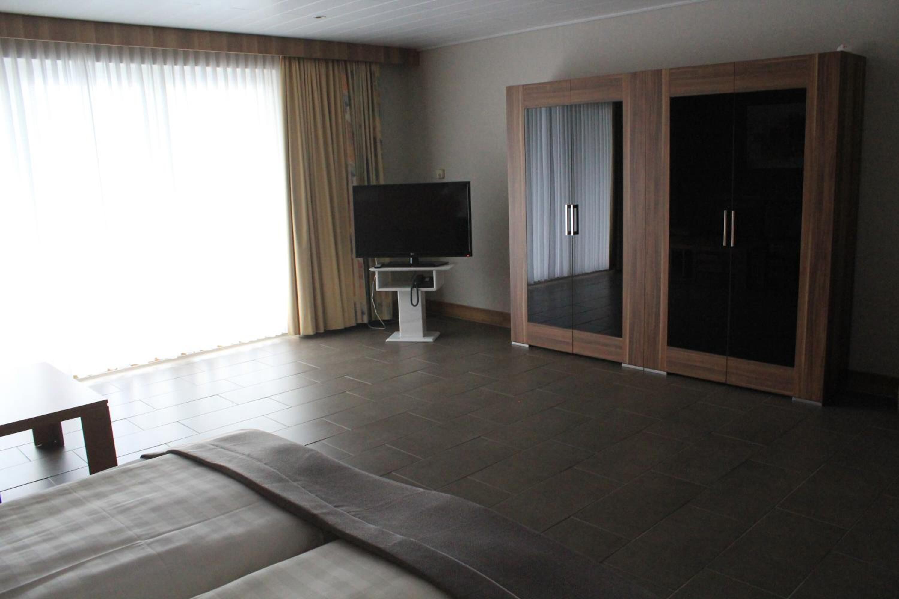 A hotel room with a large wardrobe, a flat-screen TV, a sofa, and a dining table.