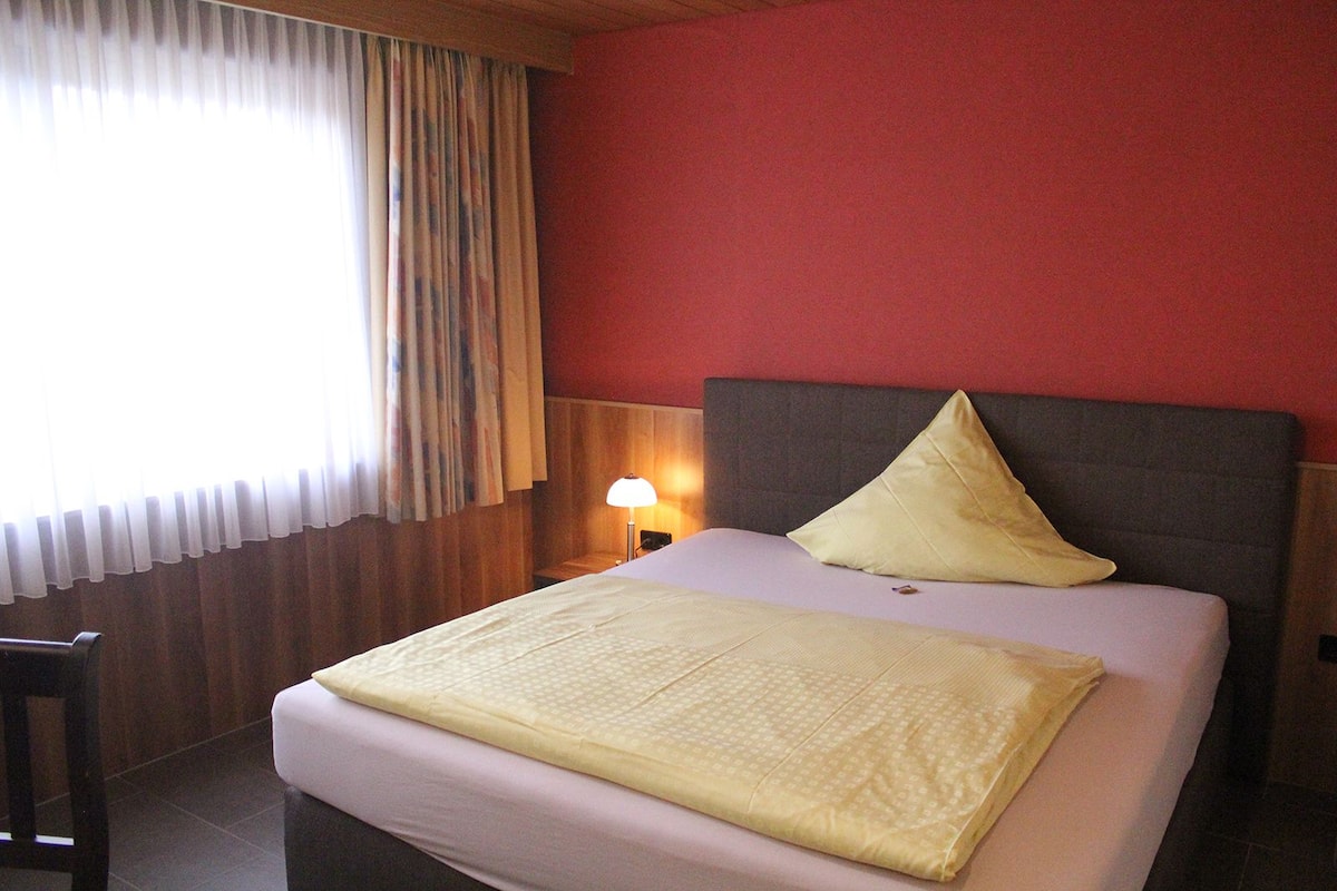 Une chambre d’hôtel avec un lit, une table de chevet, une lampe et une fenêtre avec des rideaux.