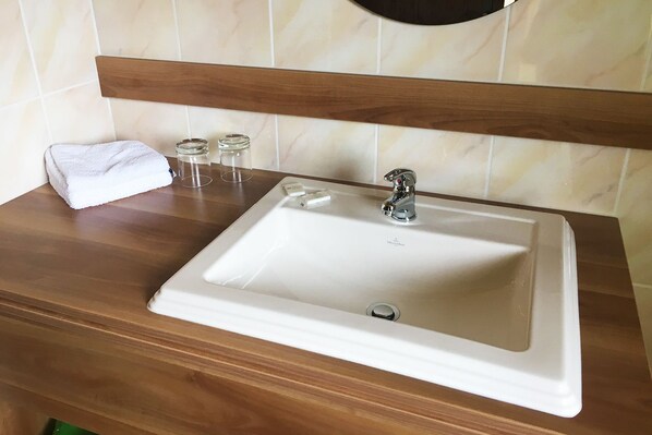 Un baño con lavamanos blanco, encimera de madera y un espejo sobre el lavamanos.