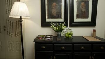 Una habitación con un aparador negro, una lámpara, cuadros enmarcados y un florero con flores.