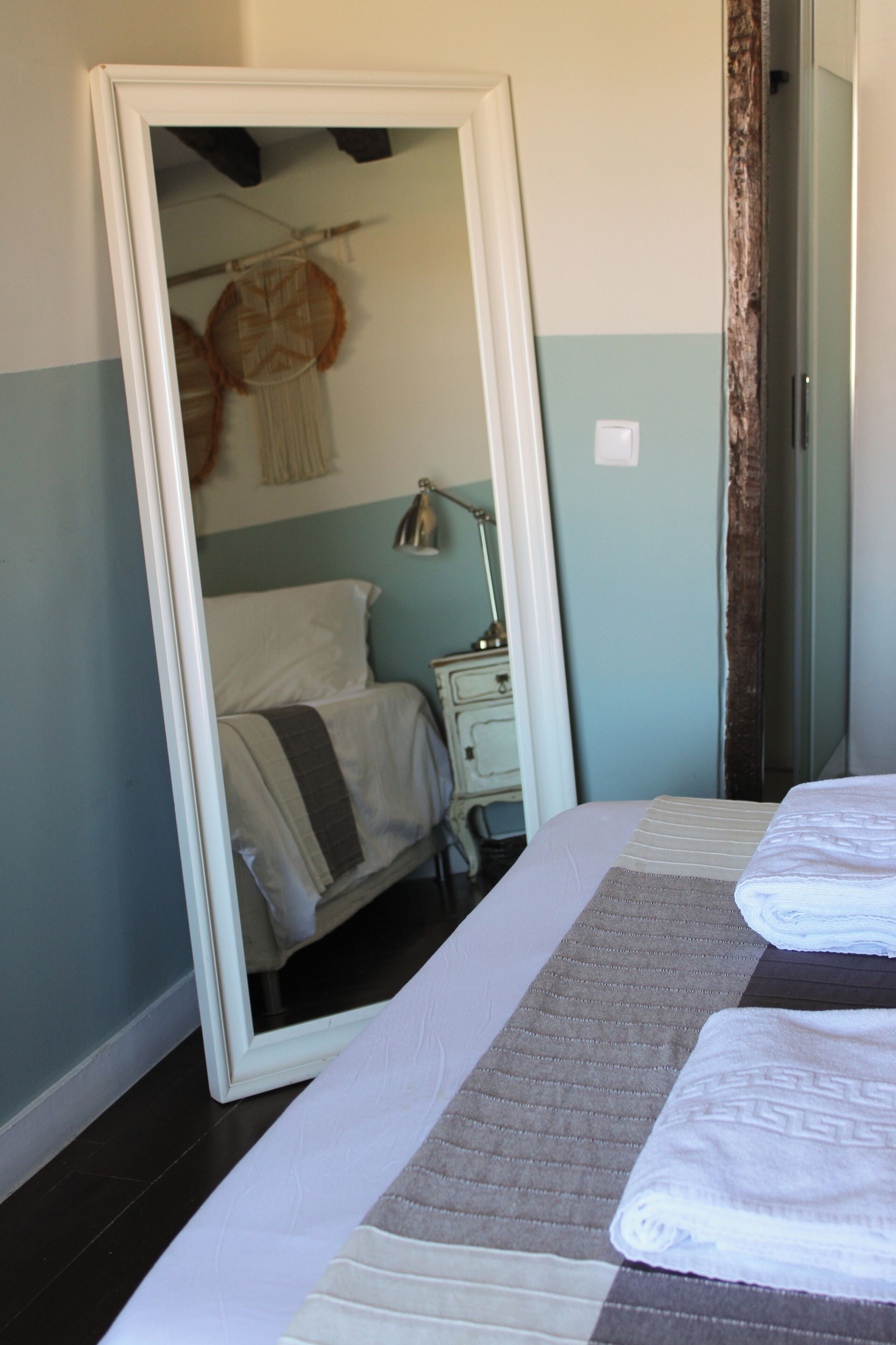 A bedroom with a bed, a nightstand, a mirror, and a wall-mounted lamp.