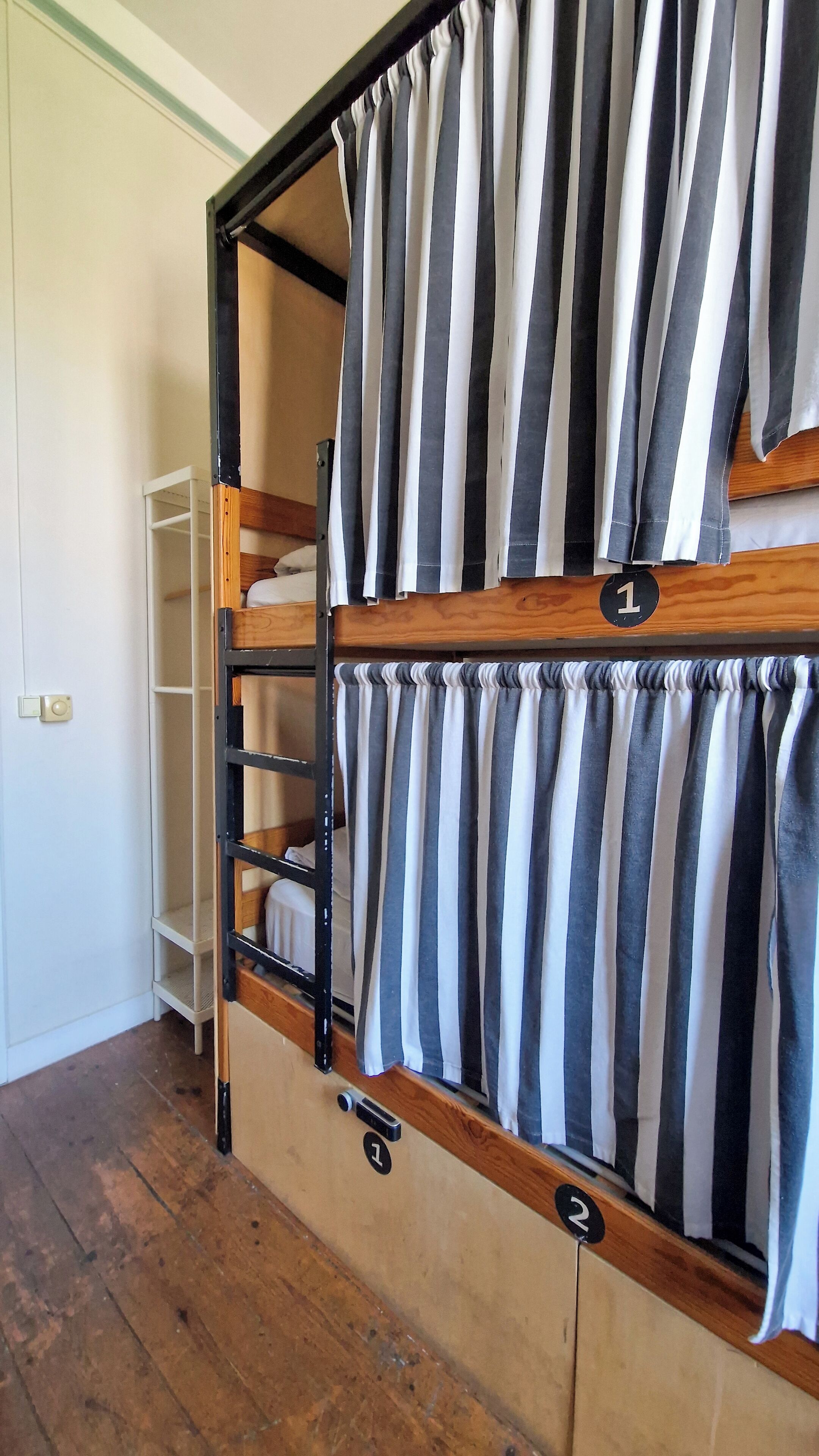 A bunk bed with striped curtains, a wooden ladder, and a white shelf unit.