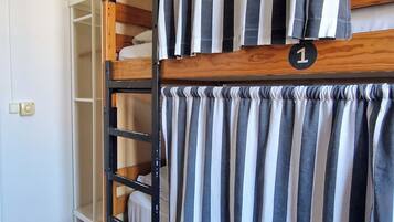 A bunk bed with striped curtains, a wooden ladder, and a white shelf unit.