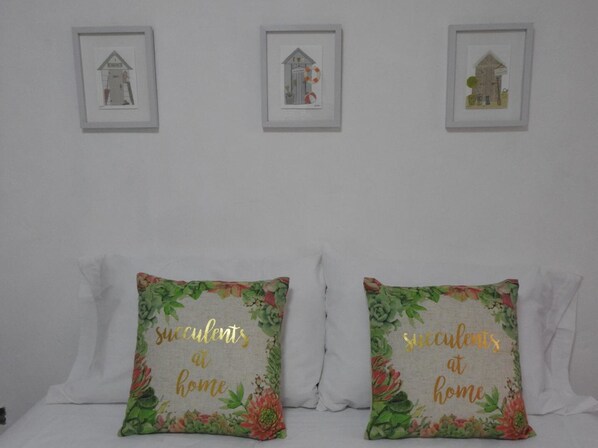 A bedroom with two decorative pillows on the bed, each with a floral pattern and the text "succulents at home". There are three framed pictures on the wall above the bed. - Casa Nava (Chetumal)