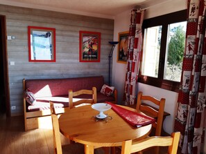Une pièce chaleureuse avec une table en bois, des chaises, un canapé rouge et deux affiches encadrées au mur.