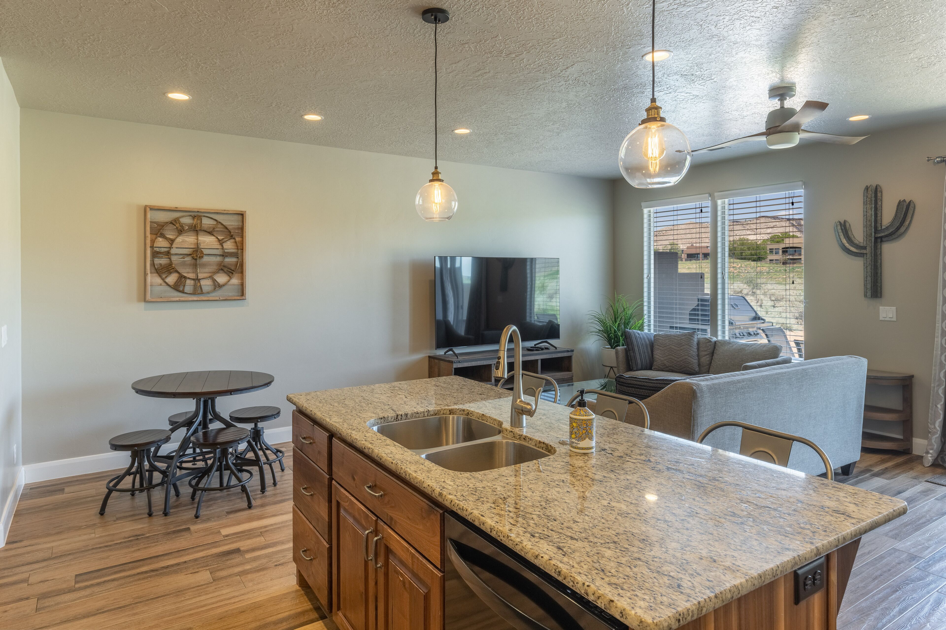 A kitchen with granite countertops, a built-in dishwasher, and a dining area with a round table and four stools.