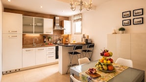 A modern kitchen with white cabinets, a dining area with a glass table, and a chandelier. - Domus Claudia - Holiday Homes (Siracusa)