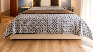 A bedroom with a herringbone-patterned wall, a patterned bedspread, and a nightstand with a lamp. - Domus Claudia - Holiday Homes (Siracusa)