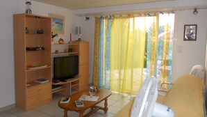Ein Wohnzimmer mit Fernseher, Holzregalen, einer Couch und einem Ventilator.