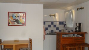 Eine kompakte Küche mit Essbereich, ausgestattet mit einem Holztisch und Stühlen, einer Kaffeemaschine und einer gefliesten Rückwand.